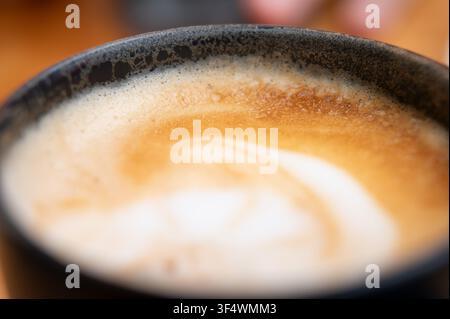 Extrem Nahaufnahme von cremigem Cappuccino-Schaum, der zarte Blasen, Milchschaum und eine strukturierte Kaffeoberfläche mit geringer Schärfentiefe zeigt Stockfoto