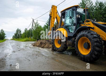 Baggerlader, der nach Regenfall auf einer Wohngebietsstraße auf einer Baustelle für Straßenarbeiten geparkt ist. Konzept: Straßenbau Stockfoto