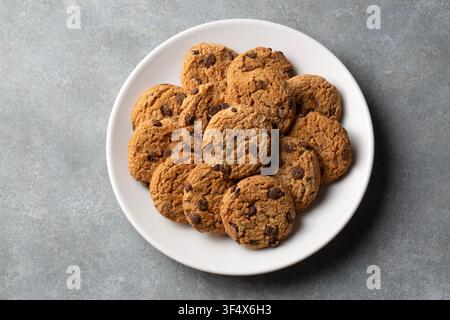 Oberblick auf Schokoladenkekse, die auf einem weißen Teller über grauem Hintergrund serviert werden Stockfoto