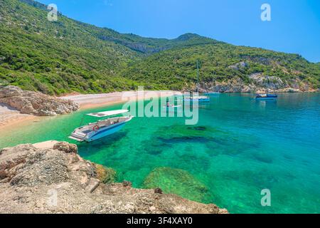 Adriatisches Meer am Strand Sveti Ivan auf der Insel Cres, Kroatien, mit türkisem Wasser, das die leuchtend grünen Hügel reflektiert, und mehreren Booten, die in der Nähe vor Anker liegen Stockfoto