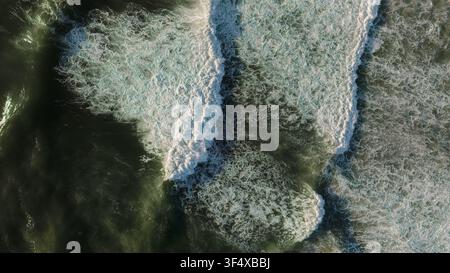 Eine Luftaufnahme von sanft rollenden Meereswellen, die mit weißem Schaum und strukturiertem dunklem Wasser am Meer brechen Stockfoto
