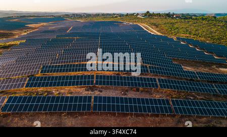 Luftaufnahme einer ausgedehnten Photovoltaikanlage, umgeben von ländlicher Vegetation und fernen Hügeln im warmen Abendlicht. Stockfoto