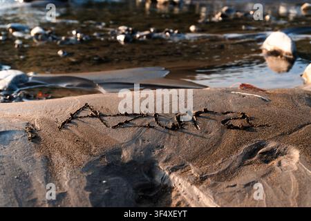 Ansicht von oben des weiblichen Namens „Azura“, der während des warmen goldenen Lichts der Goldenen Stunde in nassen Strandsand geschrieben wurde. Stockfoto