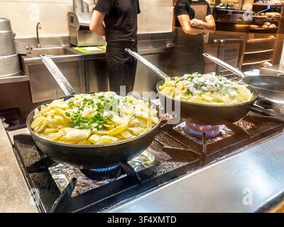 Geschnittene Kartoffeln, Zwiebeln und grüne Paprikaschoten brühen in Öl in einer Bratpfanne auf einem Gasherd in einer Profiküche. Stockfoto