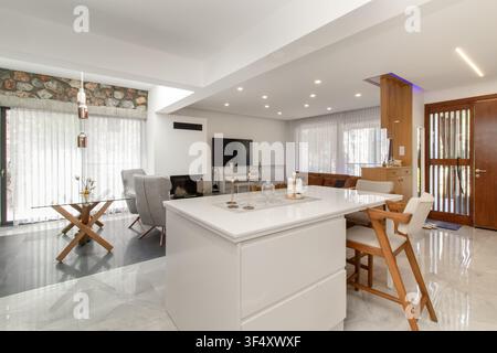 Modernes Loft-Style-Luxusvilla-Interieur mit einer weißen Kücheninsel mit Barhockern, einem Kamin und zeitgenössischen skandinavischen Möbeln Stockfoto