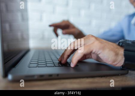 Seitliche Nahaufnahme der Hände eines Mannes, der auf einer grauen Laptop-Tastatur tippt. Ein Finger drückt eine Taste, während der andere unscharf im Hintergrund zeigt Stockfoto