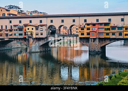 Florenz, Italien - Mai 2026: Historische Ponte-Vecchio-Brücke mit farbenfrohen Geschäften und Vasarigang, die sich im Arno spiegeln Stockfoto