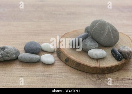 Natürliche Meereskiesel häufen sich auf rundem Holzscheibenhintergrund. Stockfoto
