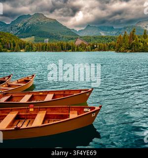Traditionelle Holzruderboote auf dem Štrbské pleso See mit dramatischen Sturmwolken und den Hochtatra-Bergen im Hintergrund, Slowakei. Stockfoto