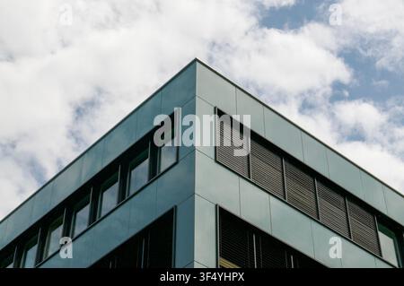 Niedrigwinklige Perspektive des scharfen Eckes eines zeitgenössischen Bürogebäudes mit dunkelgrüner Metallfassade und Glasfenstern Stockfoto