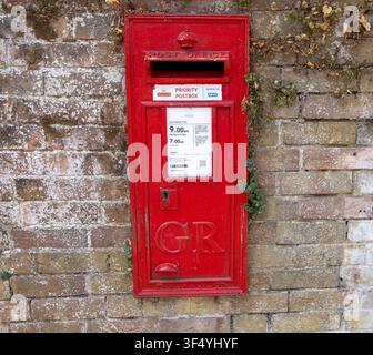 Verwitterter roter britischer wandmontierter Briefkasten mit GR-Königswappen in einer Ziegelmauer in Beaulieu, Hampshire, UK Stockfoto