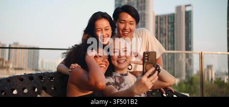 Verschiedene junge Freunde genießen den Sonnenuntergang auf dem Dach, lachen und machen ein Gruppen-Selfie Stockfoto