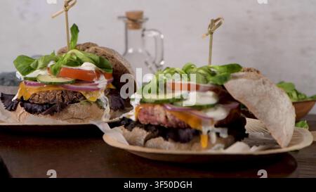 Eine Nahaufnahme zeigt zwei gestapelte vegane Bohnenburger auf kleinen Holztellern, mit geschmolzenem Käse, frischem Gemüse und Soße in r Stockfoto