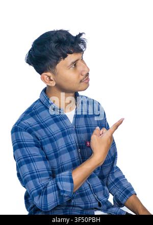 Professionelles Studio-Porträt eines fröhlichen jungen Mannes mit lockigem Haar, der mit dem Finger zur Seite zeigt und wegschaut, in einem blauen gemusterten Swea Stockfoto