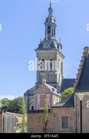 Historischer Kirchturm der Abdij van Park erhebt sich über roten Backsteingebäuden in Leuven, Belgien, eingerahmt von Bäumen und einem klaren blauen Himmel, und betont flämische Barockarchitektur und urbanen Charme. Stockfoto