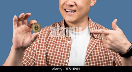 Lächelnder asiatischer Mann hält Bitcoin und zeigt Interesse an Kryptowährung, Geschäftskonzept Stockfoto