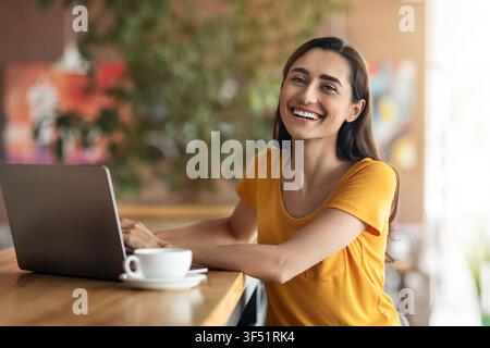 Fröhliche arabische Dame, die vor dem Laptop im Café sitzt Stockfoto