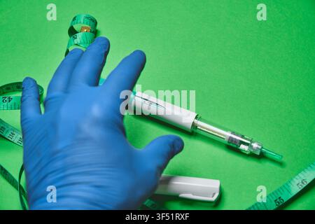 Geschützte Hand eines medizinischen Fachpersonals, die einen Injektorhalter mit einem Maßband auf grünem Hintergrund hält Stockfoto