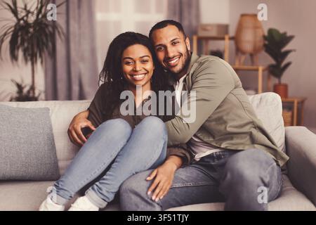 Glückliches multikulturelles Paar, das sich zu Hause auf dem Sofa umarmt, Konzept des lässigen Lebensstils Stockfoto