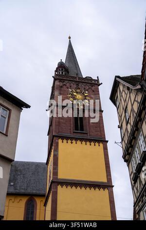 Eine Nahaufnahme eines Kirchturms mit einem großen goldenen Zifferblatt, umgeben von historischen Gebäuden unter einem bewölkten Himmel. Stockfoto
