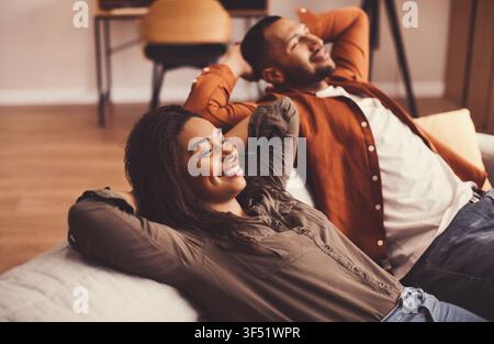 Glückliches junges Paar entspannt sich auf der Couch zu Hause, lächelt zusammen, gemütliche Inneneinrichtung Stockfoto