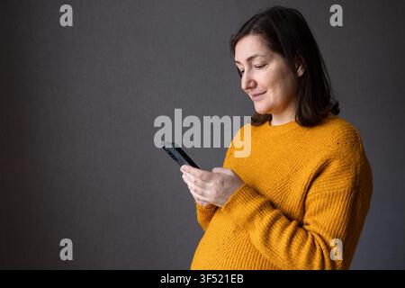 Schwangere Frau in gelbem Pullover, die ihren Bauch hält und ihn sanft mit den Händen berührt Stockfoto