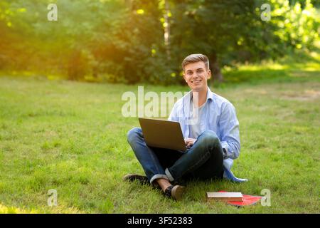 Online-Jobs Für Studenten. Lächelnder Junger Mann, Der Draußen An Einem Laptop Arbeitet Stockfoto