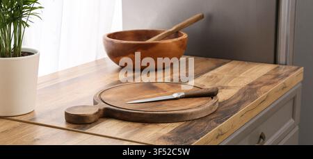 Holzschneidebrett mit einem Messer auf einer Küchenarbeitsplatte, Kochvorbereitung und Wohnraumgestaltungskonzept, eine Holzschüssel mit einem Löffel und einem Topf Stockfoto