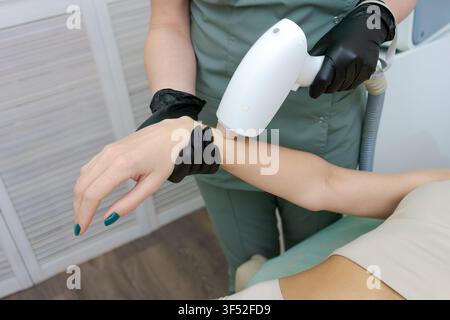 Eine Kosmetikerin in Handschuhen führt eine Laser-Haarentfernungsbehandlung am Unterarm einer Frau in einem Schönheitssalon durch, eine Epilations- und Hautpflegebehandlung Stockfoto
