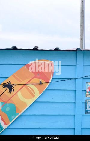 Tropischer Sommerhintergrund mit einem farbenfrohen Surfbrett und Vintage-Schildern an einer blauen Holzwand Stockfoto