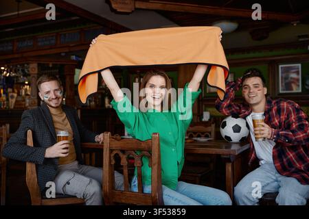 Fröhliche Gruppe von Freunden feiert ein Tor, während sie Fußball in einer gemütlichen Pub-Atmosphäre anschauen Stockfoto