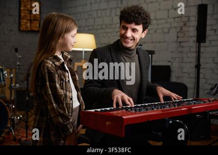 Lehrer gibt einem Mädchen am Klavier Anleitung in einer einladenden Probenumgebung Stockfoto