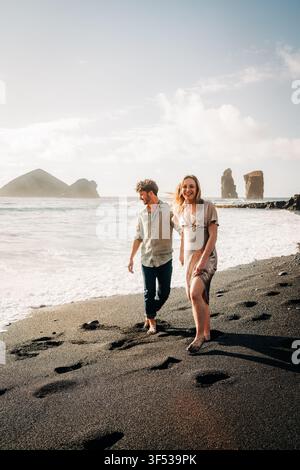 Glückliches Paar genießt einen Spaziergang an einem schwarzen Sandstrand Stockfoto
