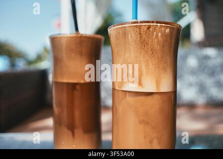 Nahaufnahme von zwei hohen Gläsern, gefüllt mit erfrischendem Eiskaffee, versehen mit dickem, cremigem Schaum oben und Strohhalmen, bereit zum Trinken in einer Café-Umgebung. Stockfoto