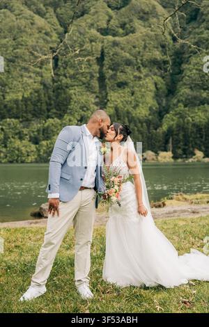 Braut und Bräutigam küssen sich an einem üppigen grünen See Stockfoto