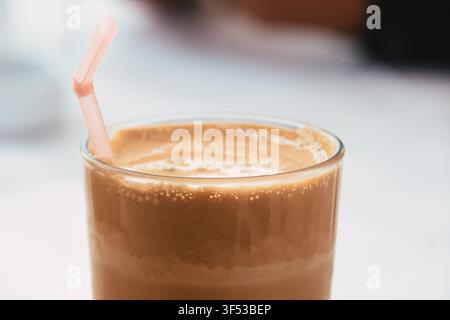 Eine Nahaufnahme eines kalten, schaumigen Eiskaffees, serviert in einem klaren Glas mit einem rosa Plastikstrohhalm, der aufrecht im köstlichen Getränk steht Stockfoto