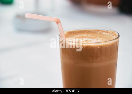 Nahaufnahme eines hohen Glases gefüllt mit einem kalten Eiskaffee-Getränk, mit einer dicken cremigen Schaumschicht oben und einem rosa Plastikstrohhalm darin Stockfoto