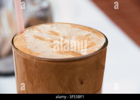 Eine Nahaufnahme eines traditionellen Eiskaffees, der in einem hohen Glas mit einem rosa Strohhalm serviert wird, mit einer dicken schaumigen Schicht oben und einem reichen braunen Getränk Stockfoto