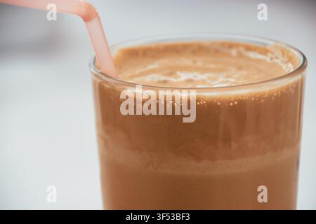 Nahaufnahme eines erfrischenden Eiskaffee-Frappé in einem klaren Glas mit einem rosa Strohhalm, mit einer dicken und cremigen Schaumschicht oben auf dem kalten Getränk Stockfoto