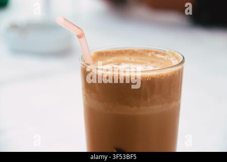 Nahaufnahme eines erfrischenden Eiskaffees in einem hohen Glas mit einem rosa Strohhalm und einer dicken schaumigen Schicht oben, kalt serviert für einen heißen Nachmittag Stockfoto