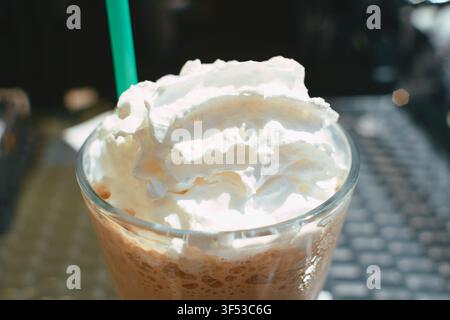 Eine Nahaufnahme eines köstlichen Eiskaffees, serviert in einem klaren Glas, reichlich mit einer Spirale aus reichhaltiger Schlagsahne und einem hellgrünen Getränk bedeckt Stockfoto