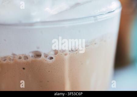 Makroaufnahme eines kalten Kaffeedrinks in einem Glas mit Schichten aus reicher brauner Flüssigkeit und einem dichten, flauschigen Sahnehäubchen, perfekt für Café-Menüs. Stockfoto