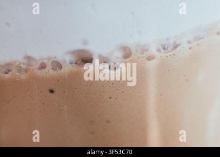 Makroaufnahme, die die detaillierte Textur von reichem braunem Kaffeecrema und zarten weißen Schaumbläschen einfängt, die auf der Oberfläche eines frisch gebrühten Heißkaffees schwimmen Stockfoto