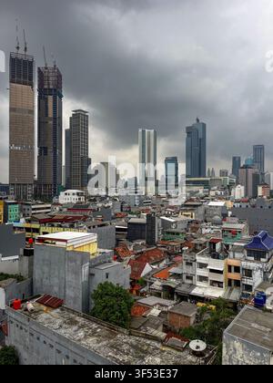 Städtischer Kontrast zwischen traditionellen Kampong-Häusern und modernen Wolkenkratzern unter einem düsteren bedeckten Himmel in Jakarta, Indonesien. Stockfoto