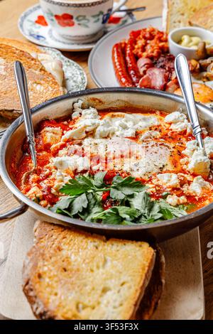 Traditionelle nahöstliche Shakshuka mit Fetakäse, serviert mit englischem Frühstück und Kaffee auf einem Holztisch Stockfoto