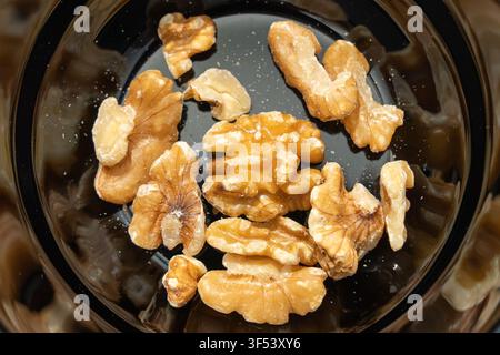Geschälte Walnuss-Hälften und -Stücke ruhen in einer dunklen Glasschale in diesem Nahaufnahme-Food-Bild. Ihre runzeligen braunen Schalen zeigen die reiche Textur dieser Pr Stockfoto