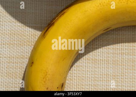 Eine reife gelbe Banane wölbt sich über ein gewebtes Tischset in diesem Nahaufnahme-Food-Foto. Kleine braune Flecken und ein dunkler Stiel heben die Textur der Stockfoto