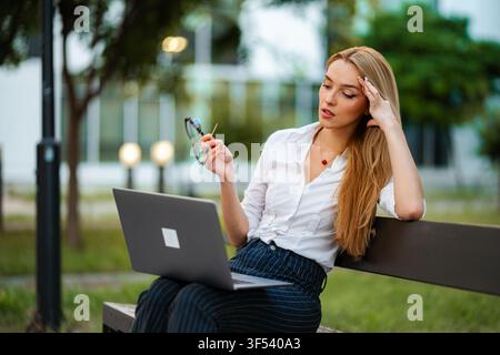 Junge erwachsene Frau fühlt sich gestresst, während sie im Freien am Laptop arbeitet Stockfoto