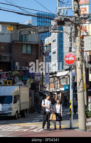 Ein junges Paar geht zusammen auf einer sonnigen Straße in Seongsu-dong, Seoul, in der Nähe eines Lieferwagens und Strommasten mit Überheadkabeln. Stockfoto