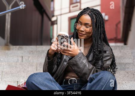 Junge Frau, die Smartphone benutzt und lächelt, während sie auf der Treppe sitzt Stockfoto